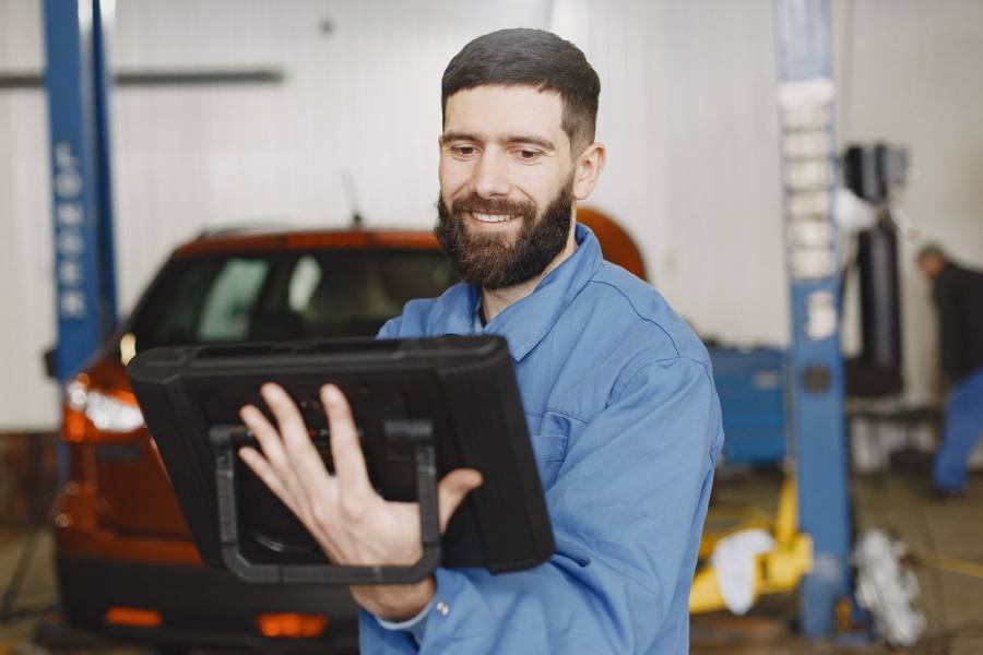 Auto technician using a tablet for vehicle records in a workshop